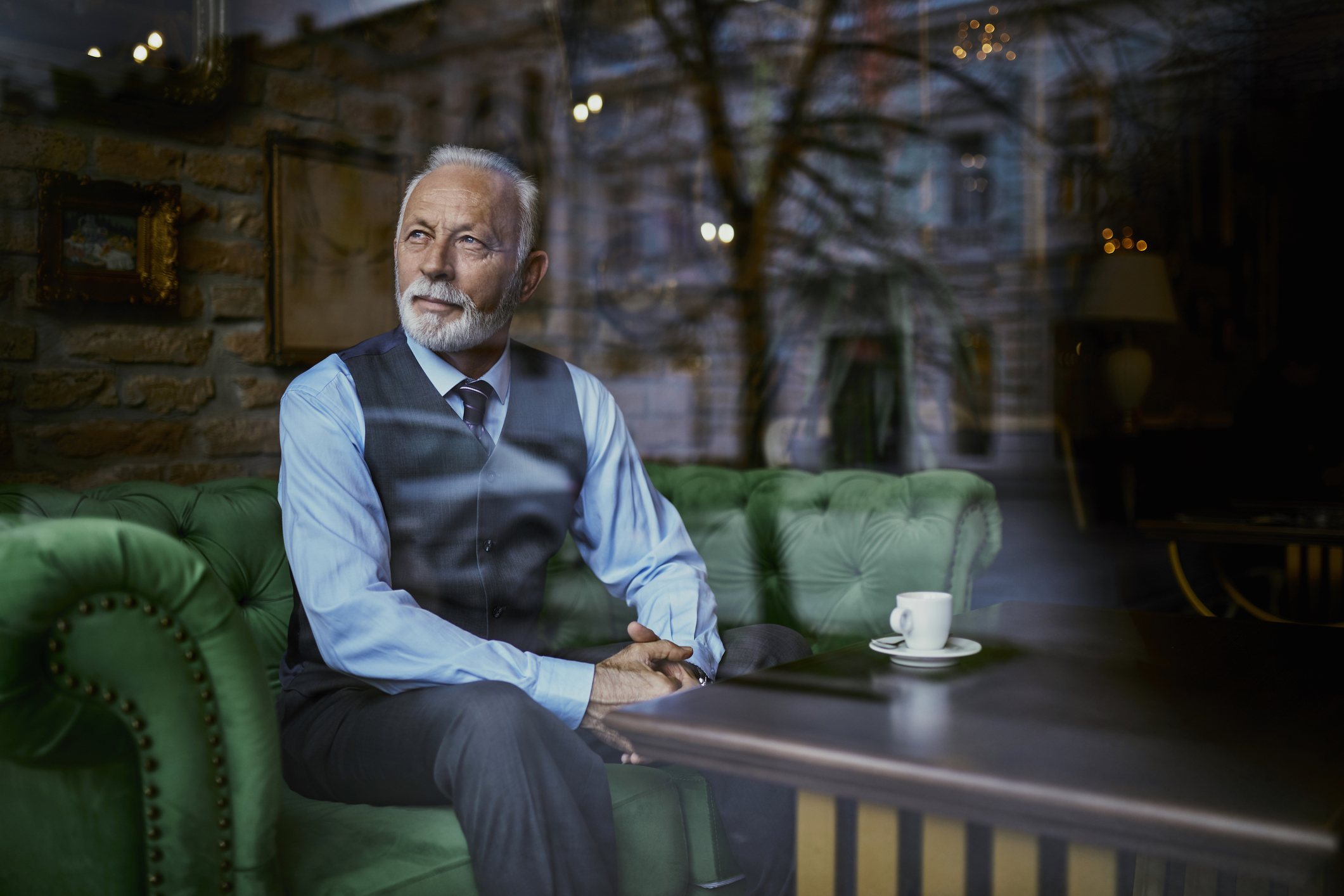 Elegant senior man sitting on couch in a cafe looking out of window
